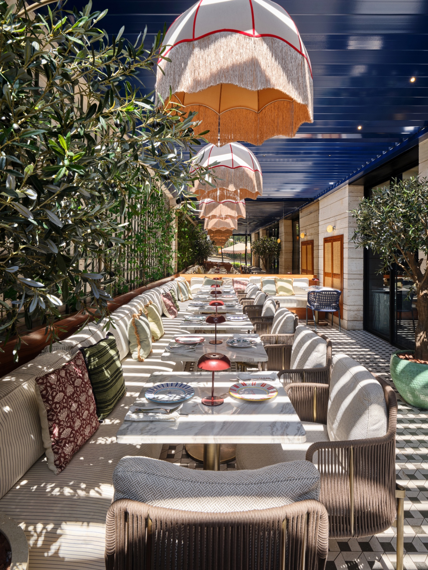 Beyti garden terrace with marble tables, woven chairs, hanging parasol lamps, and olive trees