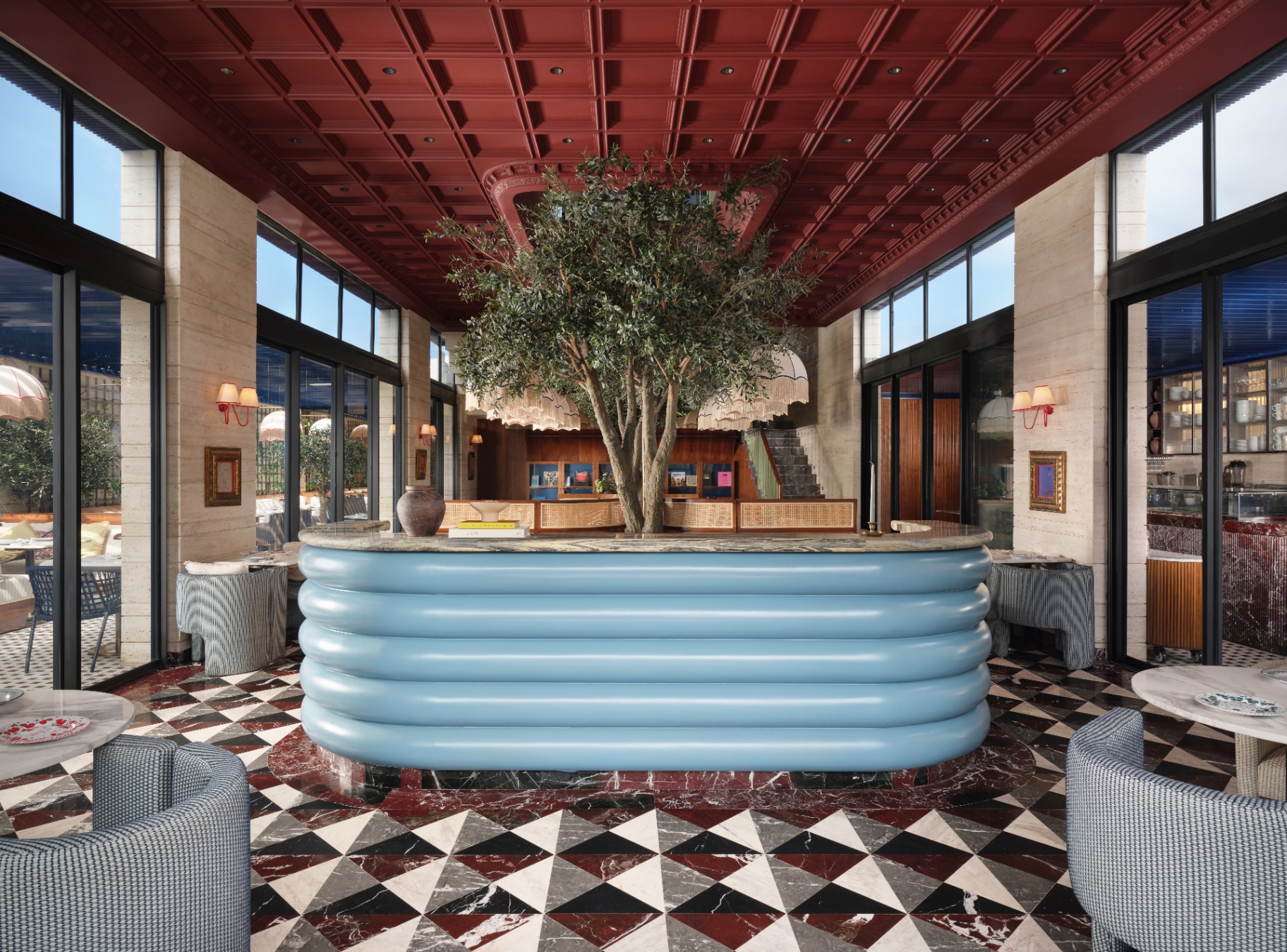 Beyti main hall with crimson coffered ceiling, central olive tree, sky-blue ribbed bar, and harlequin marble floor
